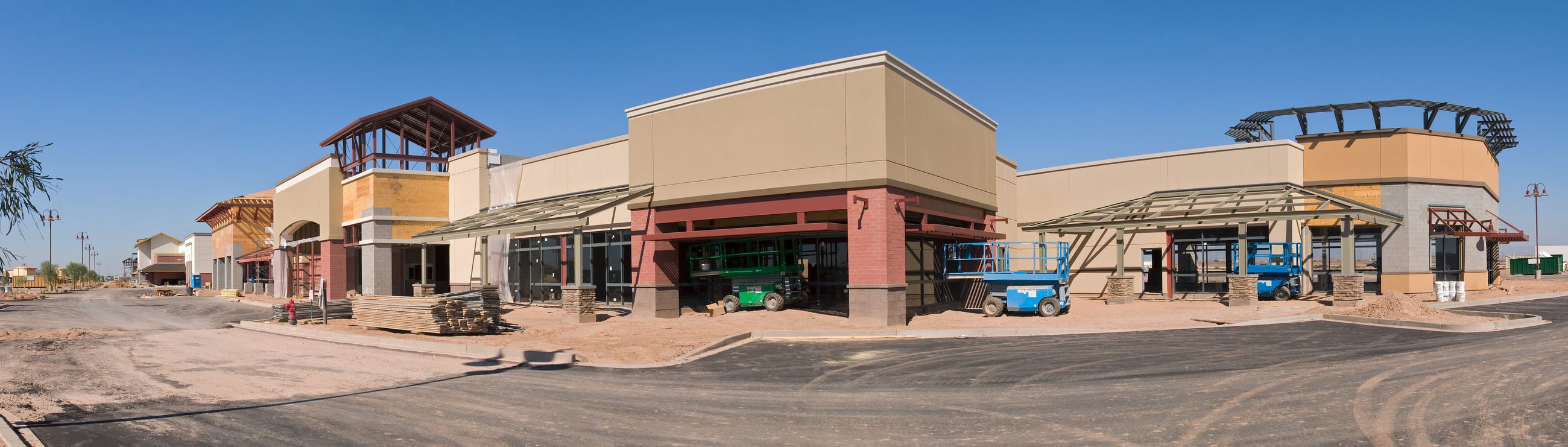A retail center mid-construction, its storefronts framed and scaffolded with equipment staged along the lot