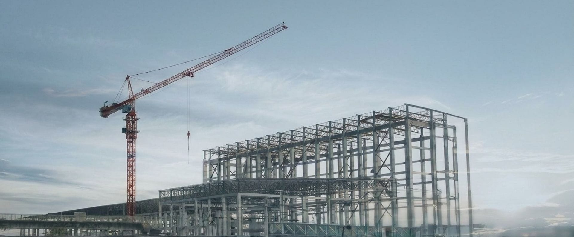 A tower crane standing beside the bare steel skeleton of a commercial building on an open site