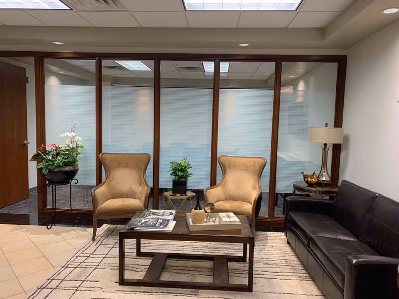 The finished Lincoln Financial waiting area — wing chairs and a leather sofa around a low table, framed by wood-trimmed glass partitions into the offices behind