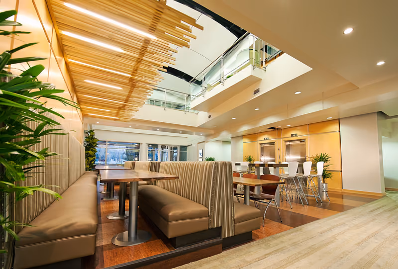 The completed Ancestry Cafe — leather banquette booths and dining tables beneath a slatted wood ceiling, opening onto a two-story atrium